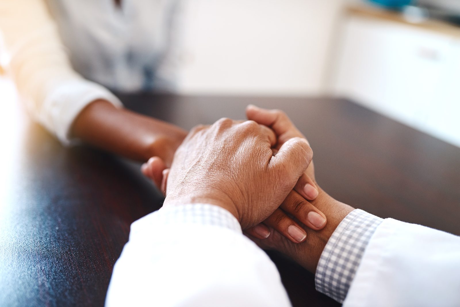A provider holding a patient’s hand across a desk