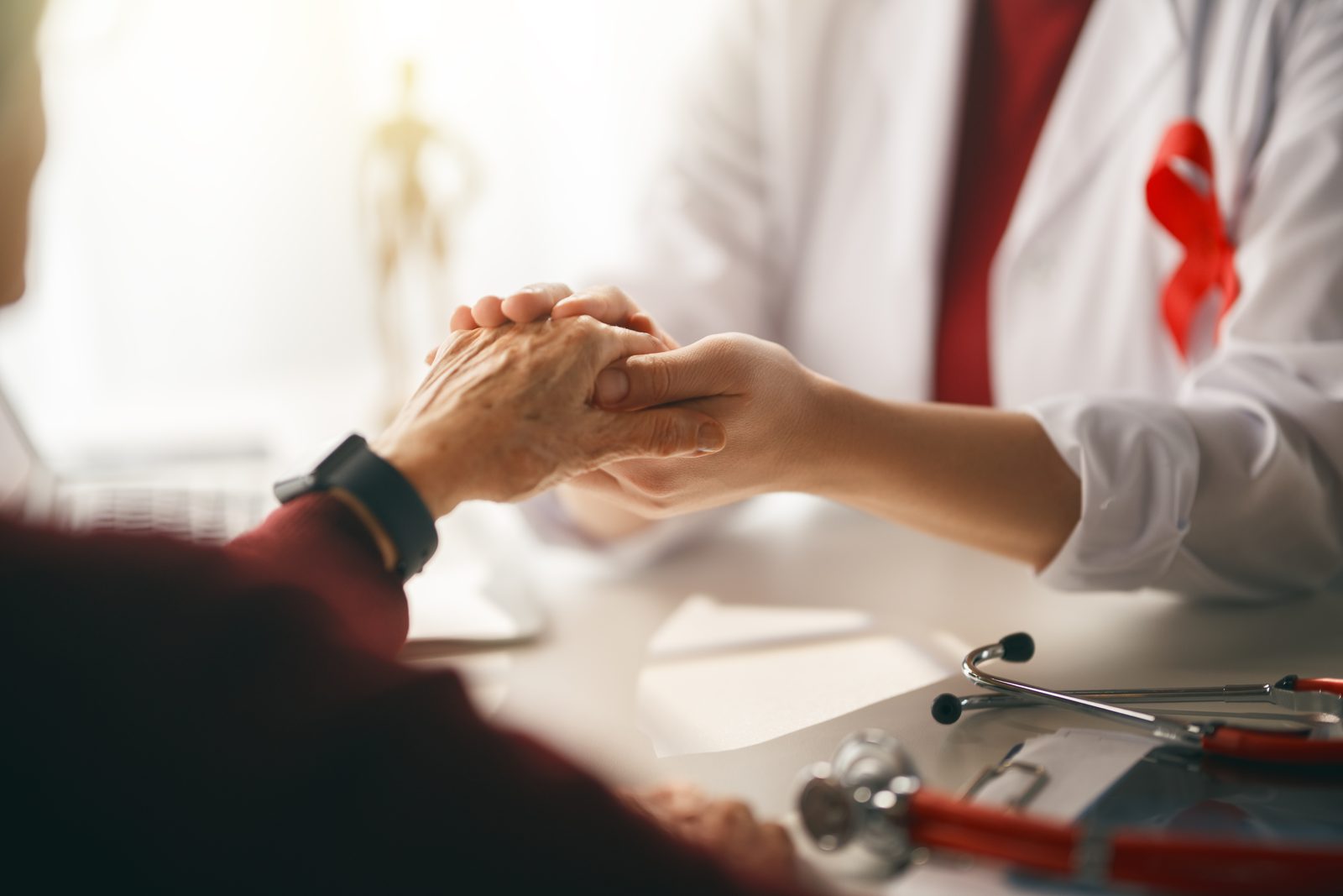 A provider holding an older patient’s hand during a visit